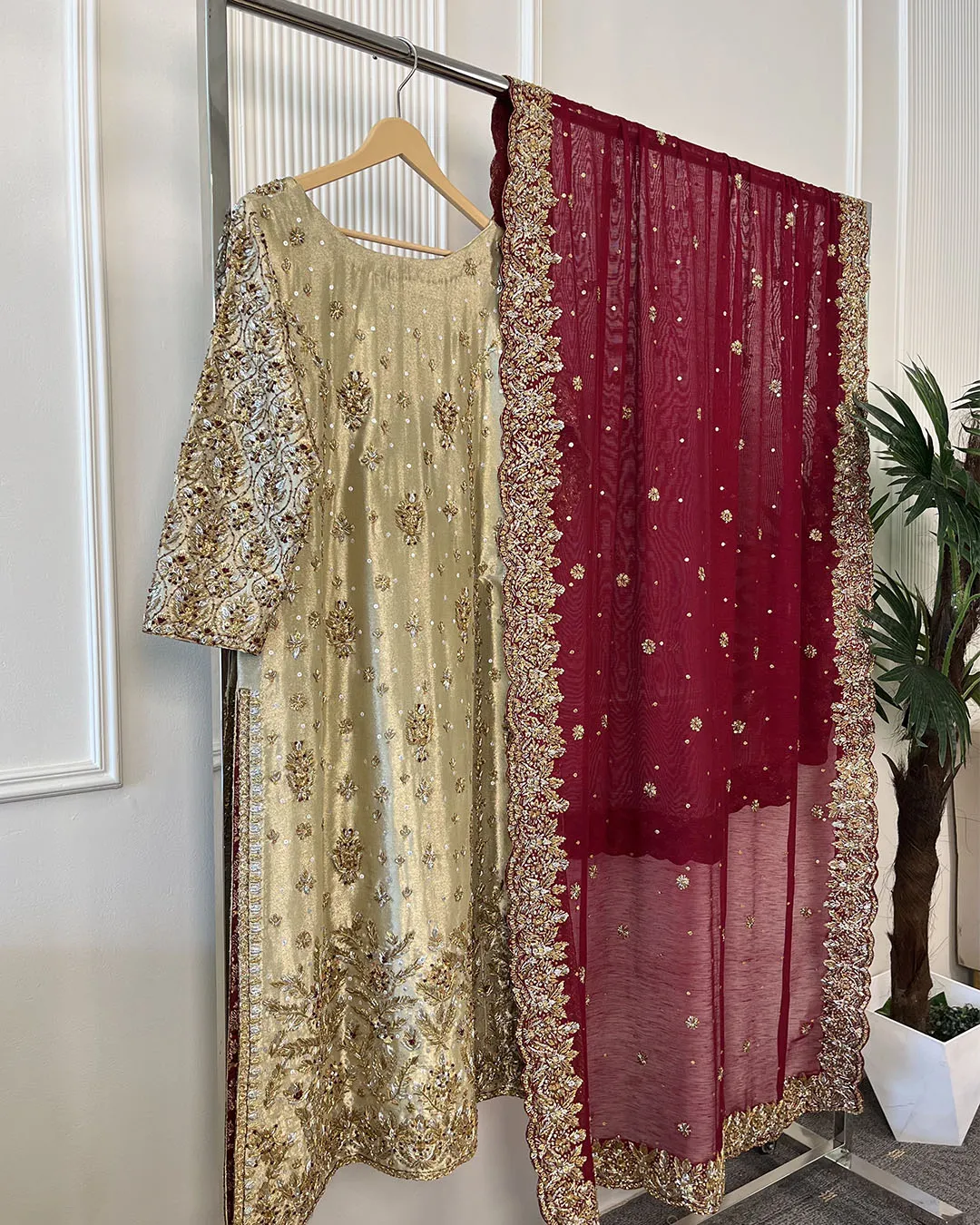 resize_0006_Document from subhan junejo (11) Full view of 3-piece gold and maroon Pakistani bridal suit on clothing rack showing embroidered kurti, heavy sleeve embroidery and maroon dupatta with gold border